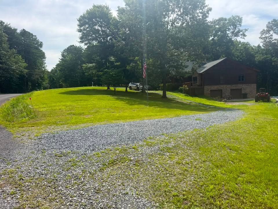 Gravel driveway through a sunny green lawn beside a small house and trees