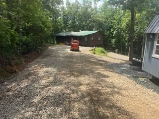 Gravel driveway with a red tractor leading to a wooded house and shed