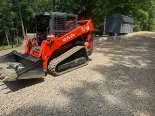 Orange Kubota compact track loader on gravel near trees and a shed