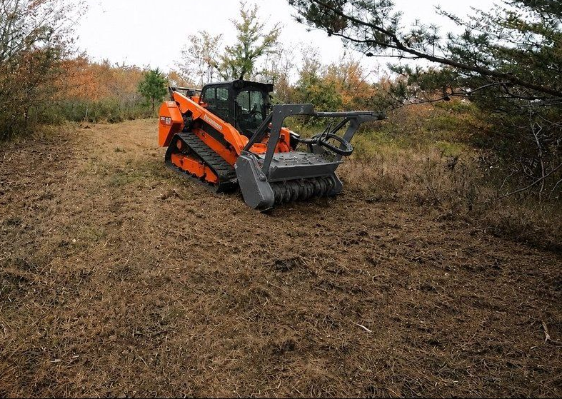 Farm road with a black tractor implement grading muddy dirt track alongside grass.