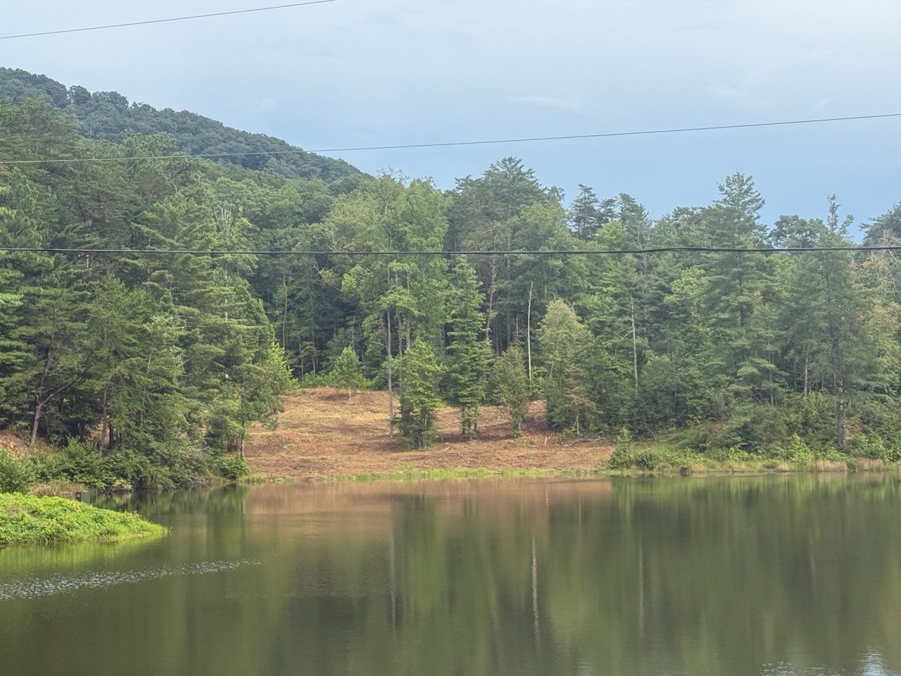 Calm lake reflecting green forested hills under a clear sky