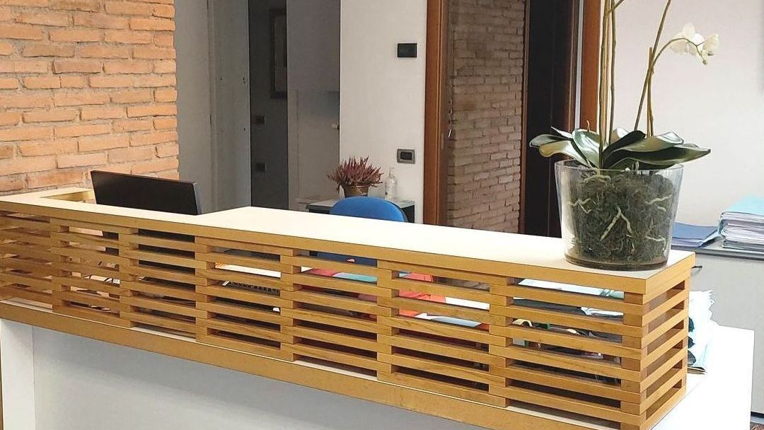 Ufficio/salotto interno con parete divisoria a doghe di legno, parete in mattoni e una pianta in vaso su un bancone.