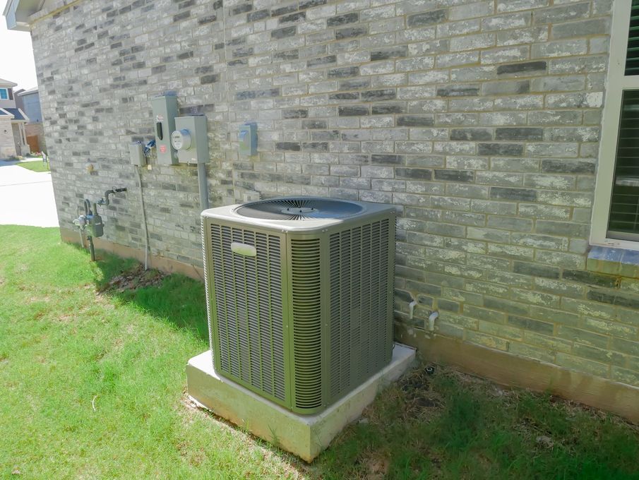 Outdoor air conditioner unit beside a stone house wall on a grassy lawn