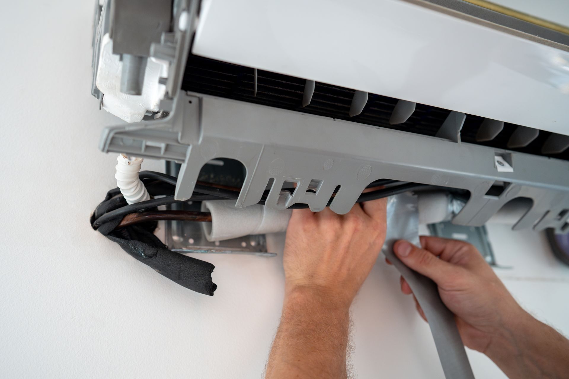 Hands installing or repairing a wall-mounted air conditioner with tools and exposed cables