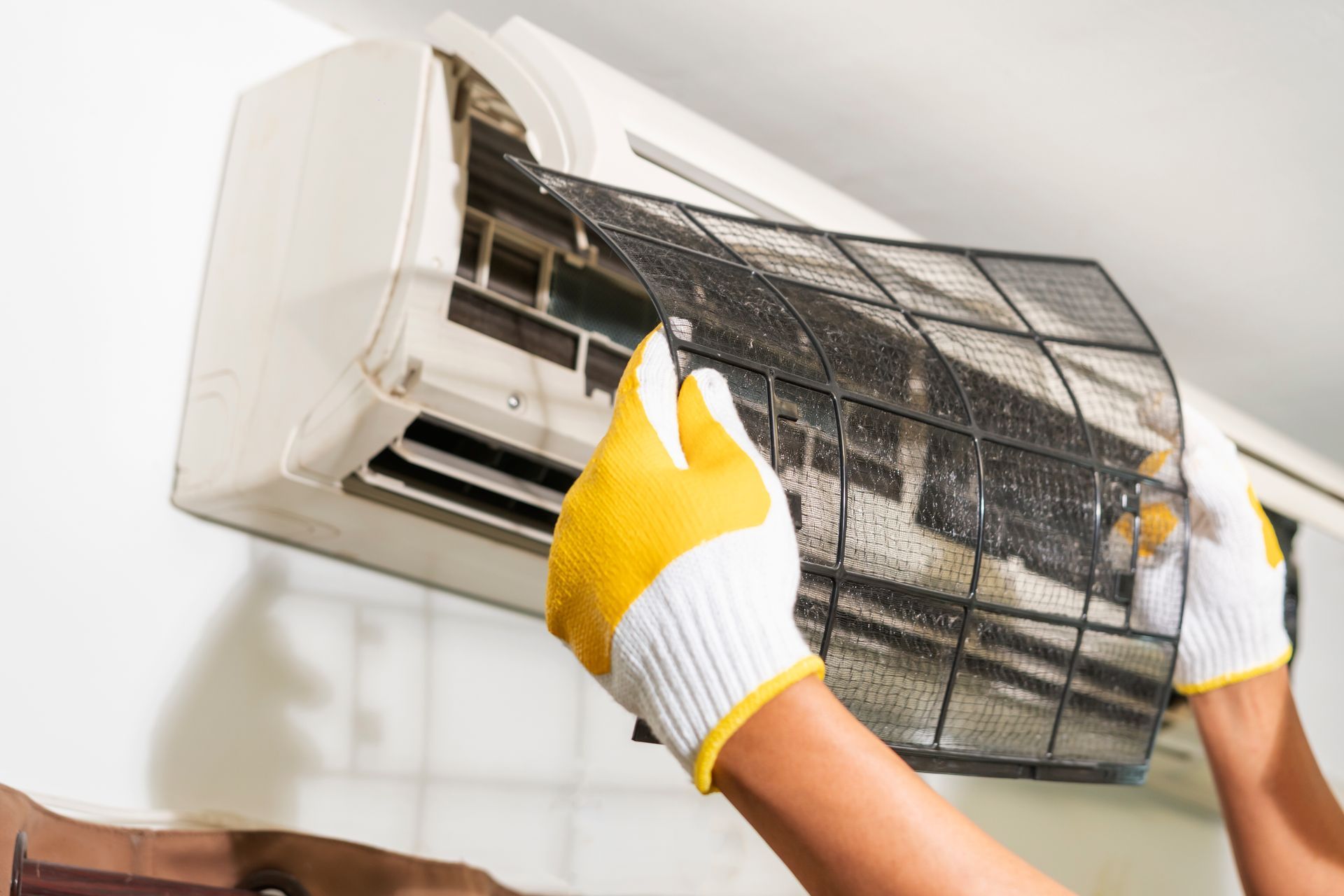 Gloved hands cleaning a wall-mounted air conditioner filter