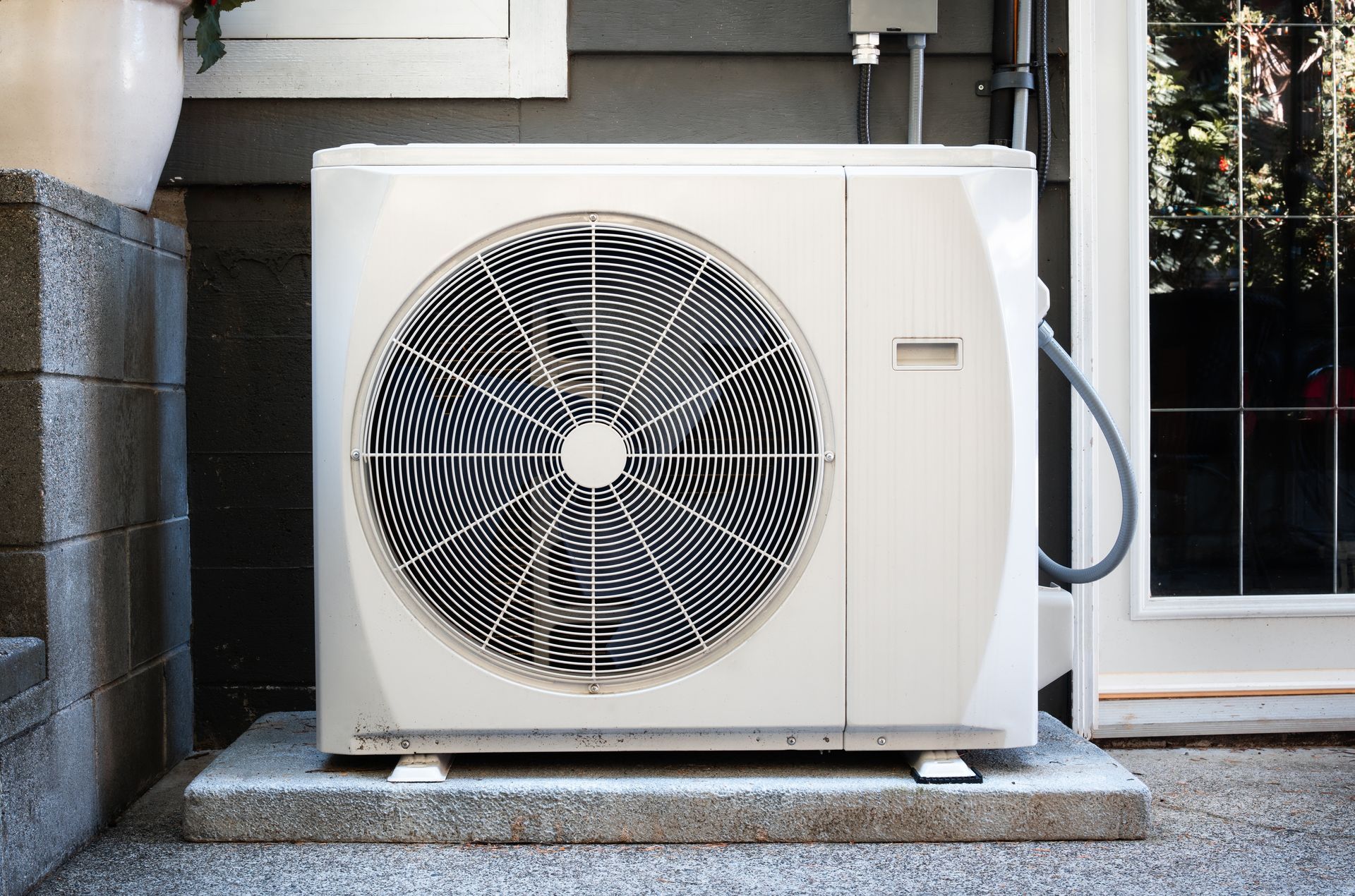 Outdoor air conditioning unit beside a house door, with a large front fan on a concrete pad.