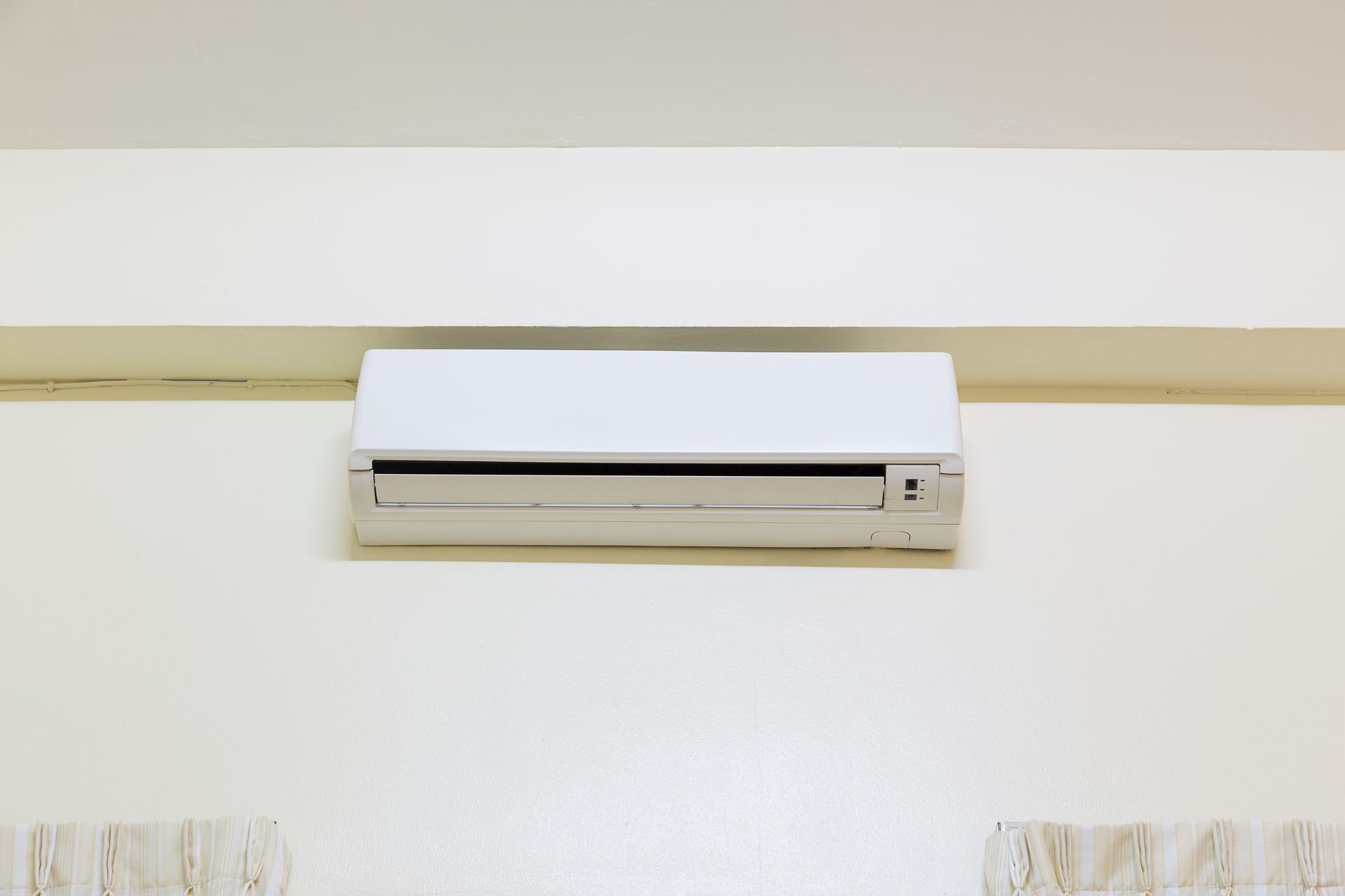 Wall-mounted white air conditioner on a beige wall