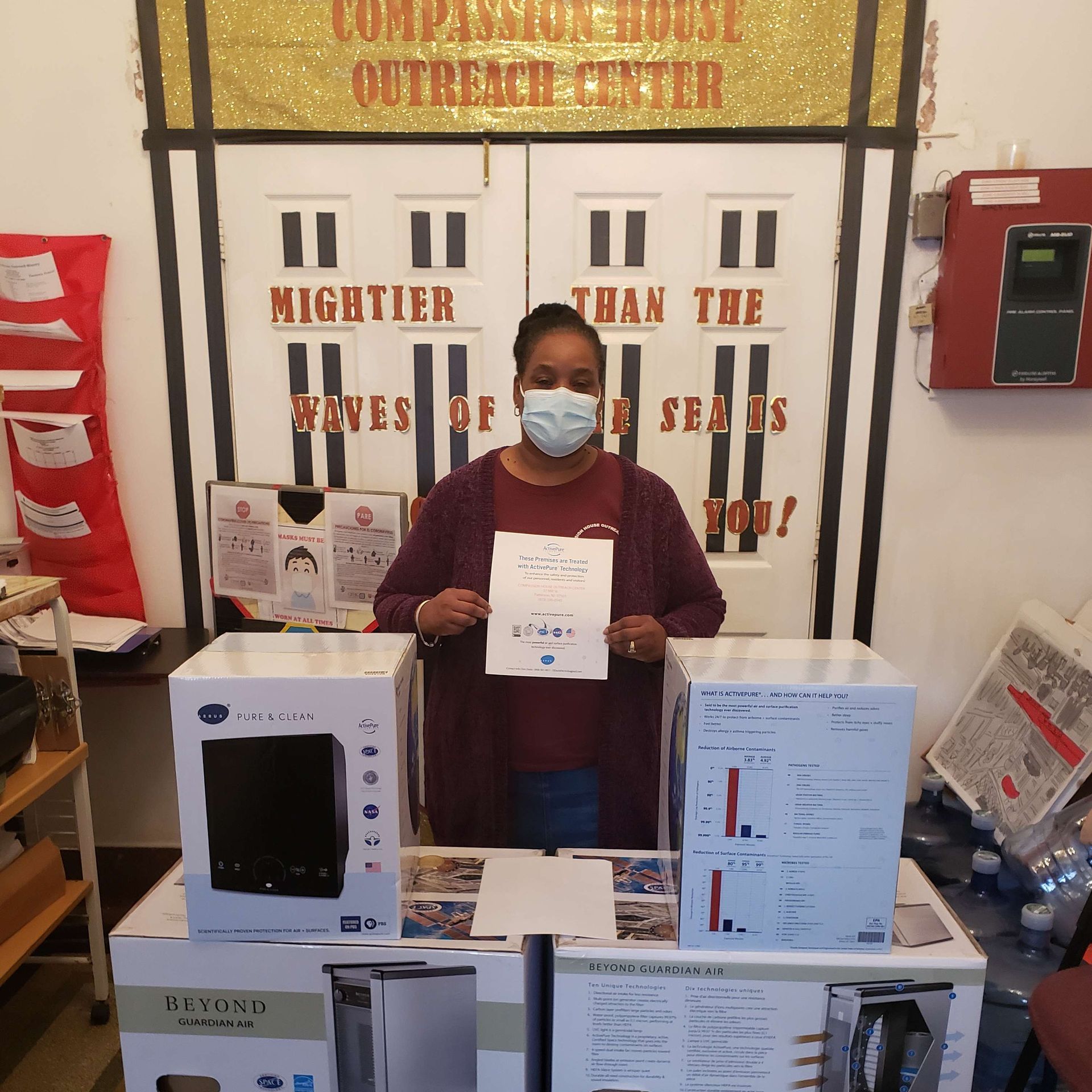 Masked person holding a certificate behind a table with boxed appliances at a trade show booth