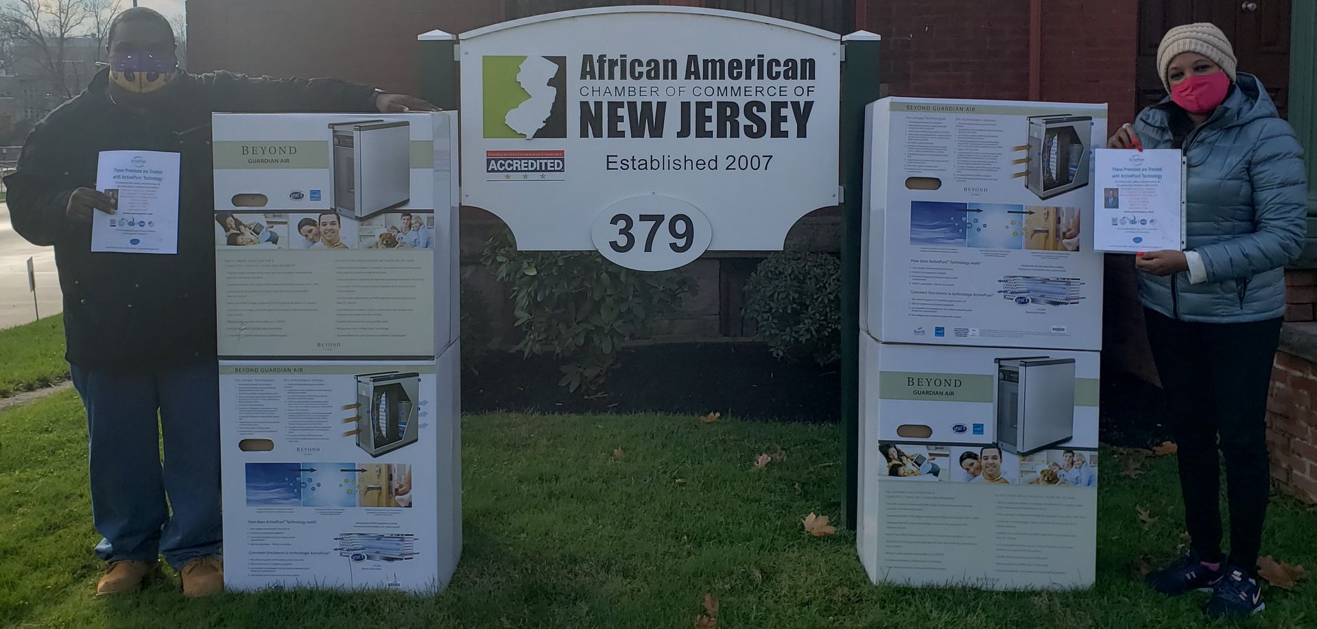 Two people beside Jersey signs and posters at a park entrance with a “New Jersey” sign and number 379.