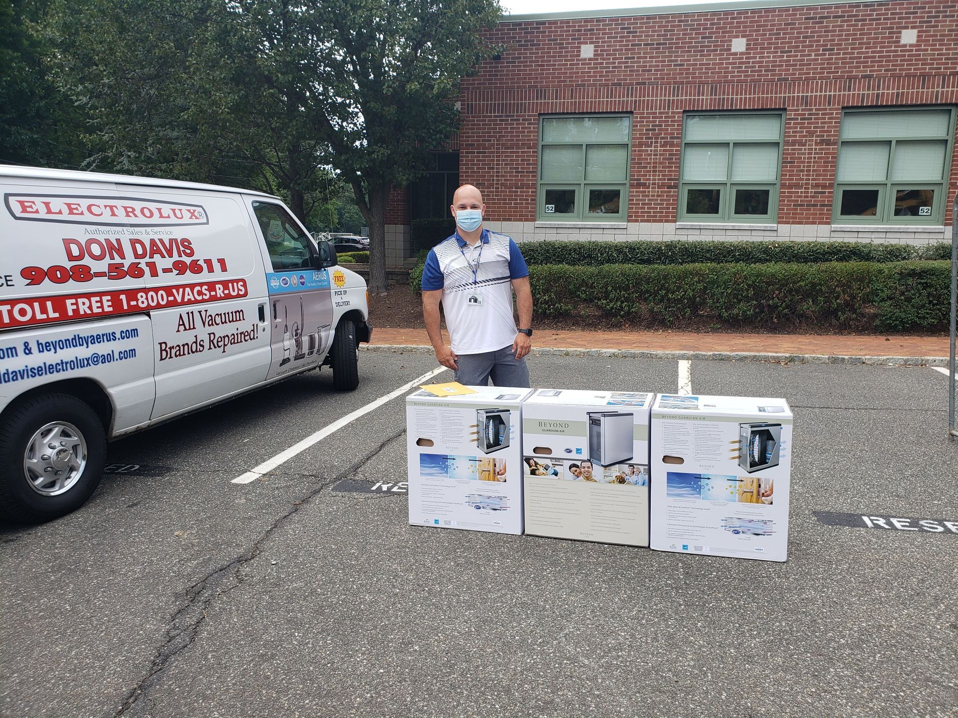 Man stands beside donation bins and a van with election campaign signs in a parking lot