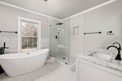 Bright modern bathroom with a freestanding tub, glass shower, and marble vanity countertops