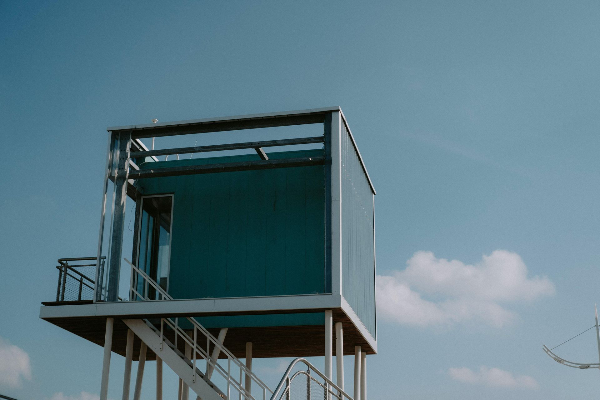 Blue lifeguard tower on stilts, with a blue sky and some clouds.