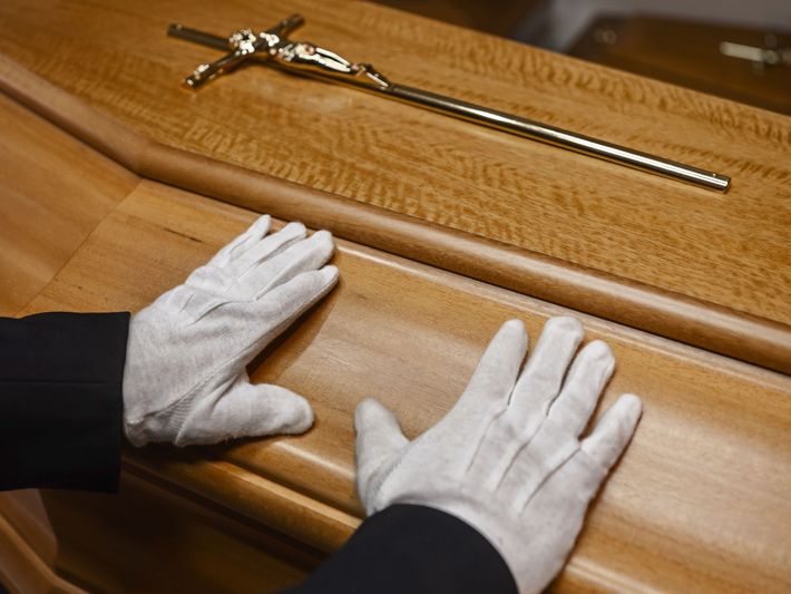 Mani guantate di bianco poggiano su uno scrigno di legno lucido accanto a una croce d'oro ornamentale.