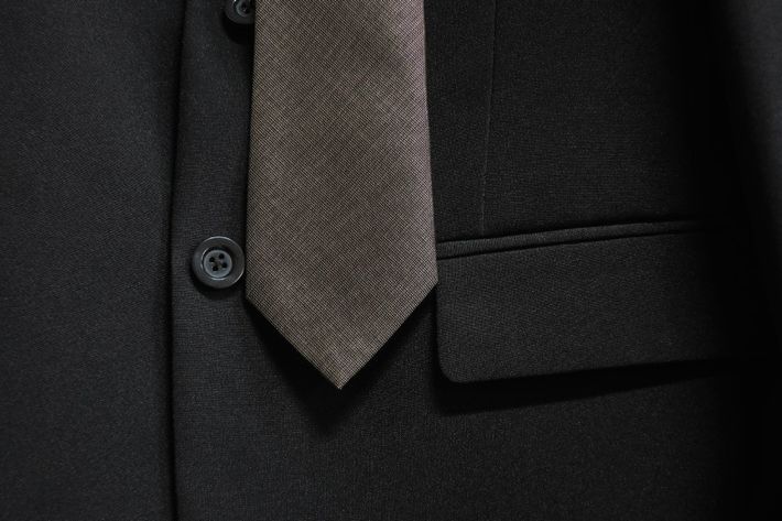 Primo piano di una giacca scura da completo con cravatta e colletto della camicia grigi a fantasia.