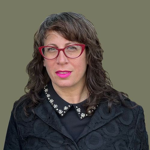 Person in a black jacket and red glasses, posing against a plain wall.
