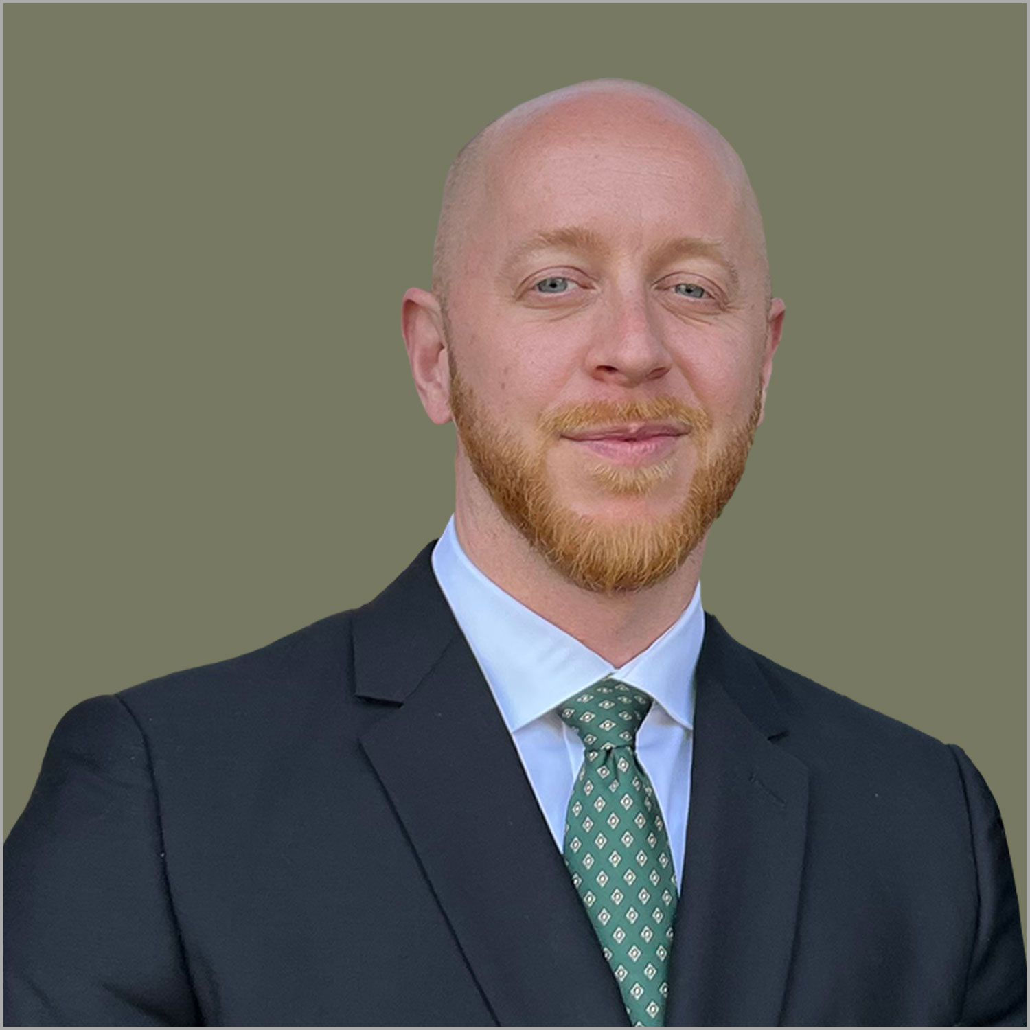 Smiling bald man in a black suit, white shirt, and green tie against a light wall.