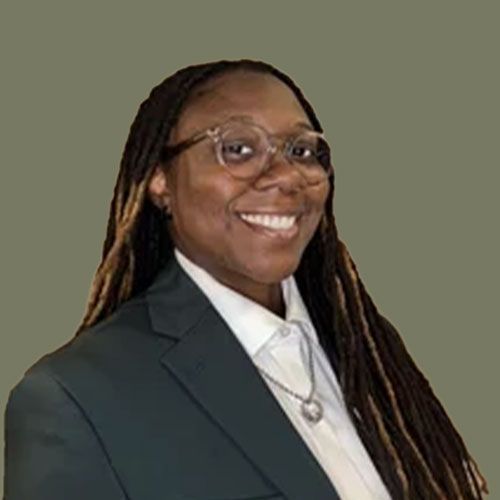 Smiling person in a dark green blazer and white shirt, wearing glasses, against a beige background