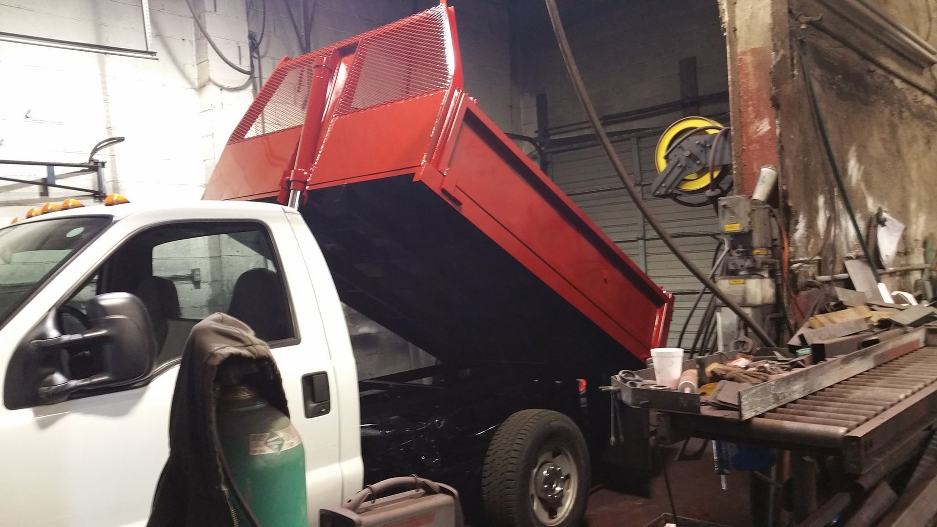 A white dump truck with a red bed is parked in a garage.