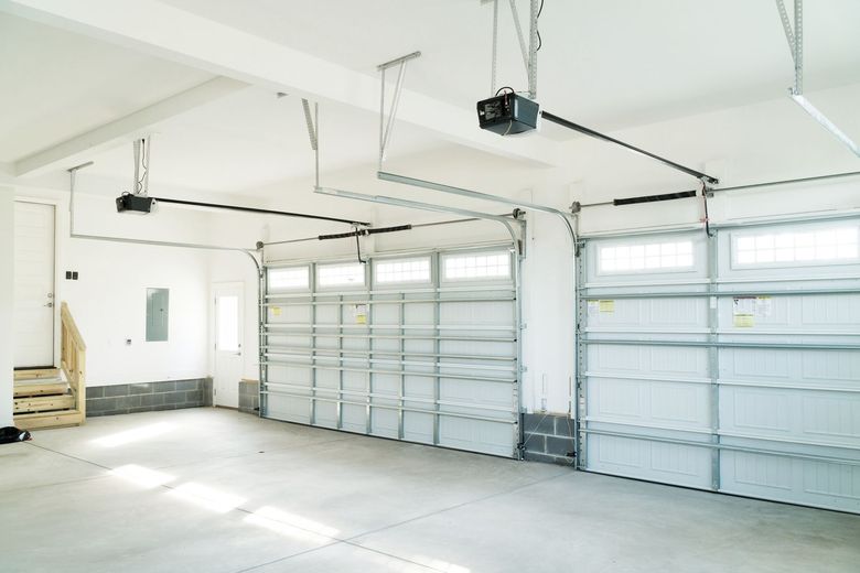 Interior view of an empty garage with two closed doors, concrete floor, white walls and ceiling.