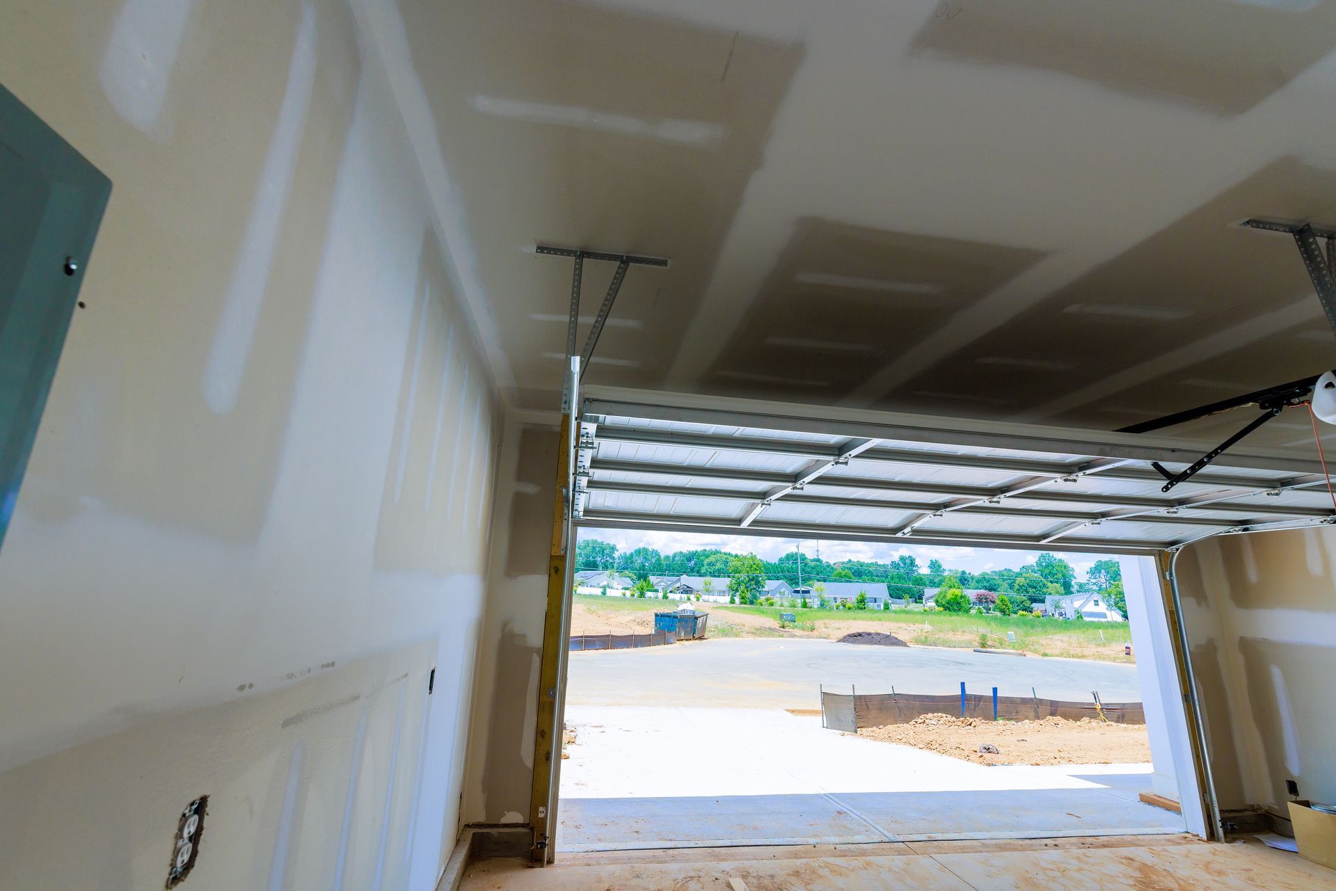 Unfinished garage interior with drywall and open doorway to outdoor view.