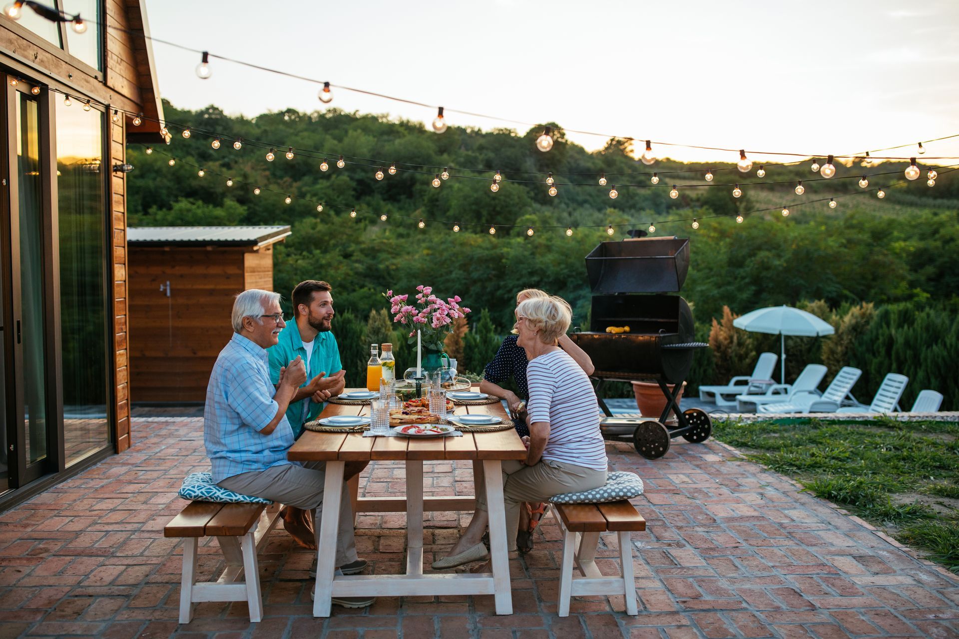 Family at an outdoor dinner table; grilling and string lights in the background.