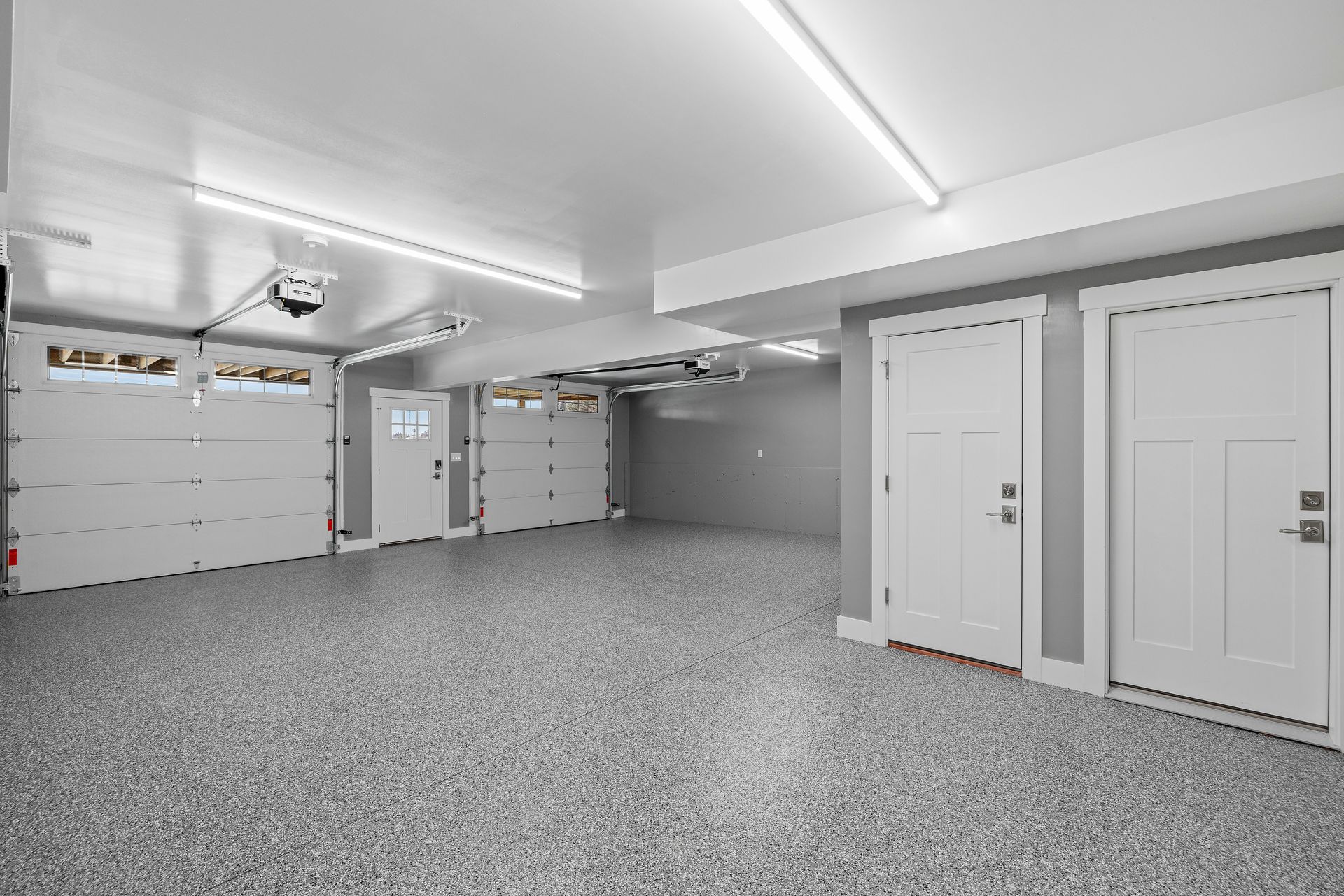 Empty, bright garage with gray speckled floor, white doors, and garage doors.