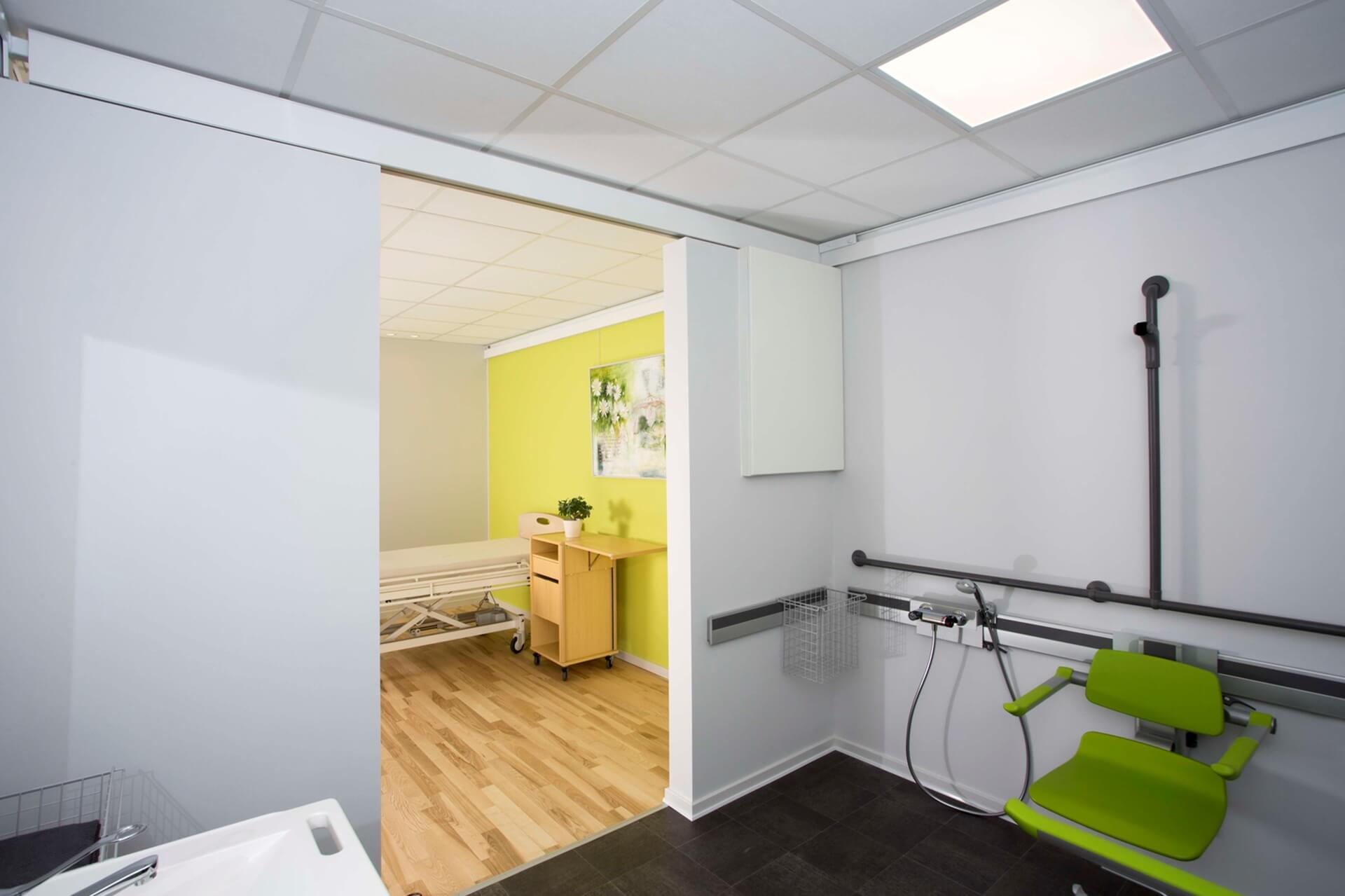 Ein Badezimmer in einem Krankenhaus mit einem grünen Stuhl und einem Waschbecken.
