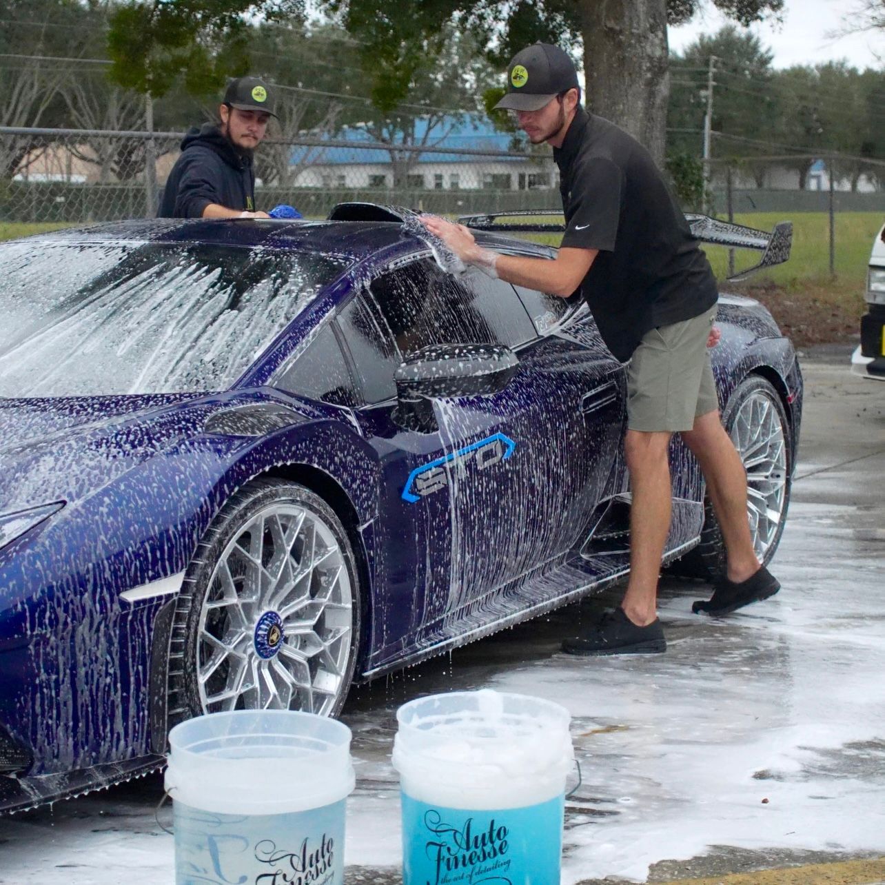 A man is washing a blue sports car in a parking lot