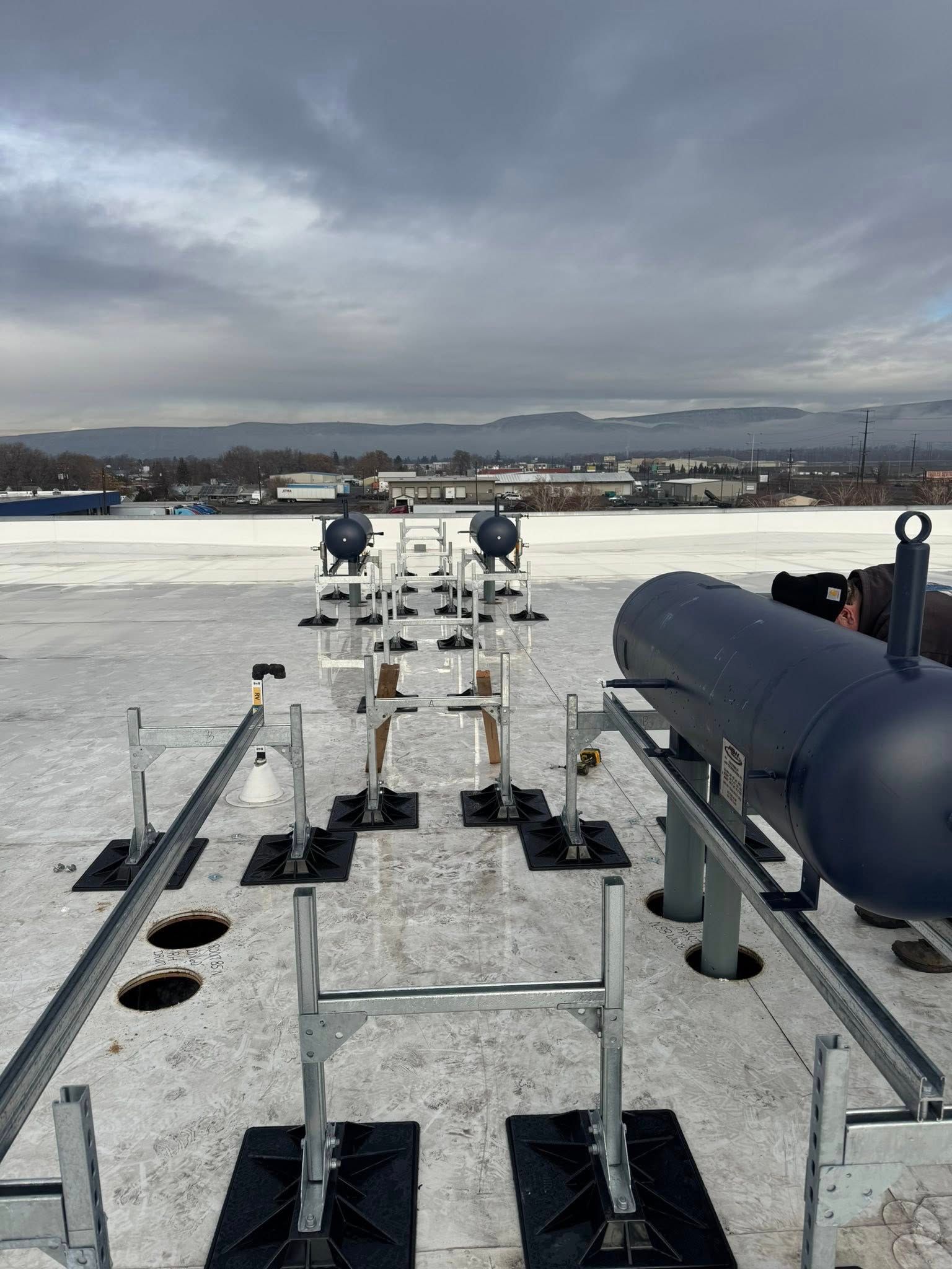 Rooftop scene with machinery and equipment; cloudy sky and cityscape in background.