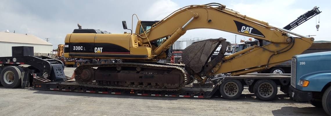 Yellow Caterpillar excavator loaded on a flatbed trailer, being pulled by a blue semi-truck.