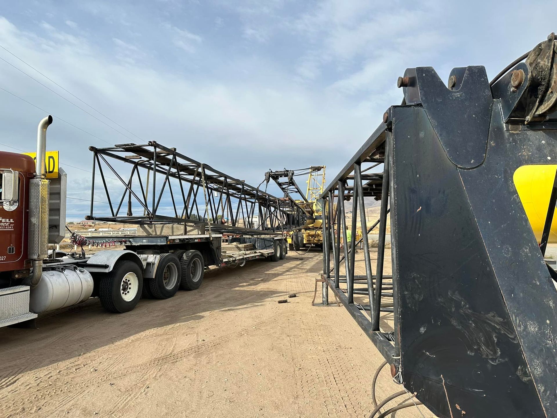 Truck carrying a large, black metal structure on a flatbed trailer in an outdoor setting under a cloudy sky.
