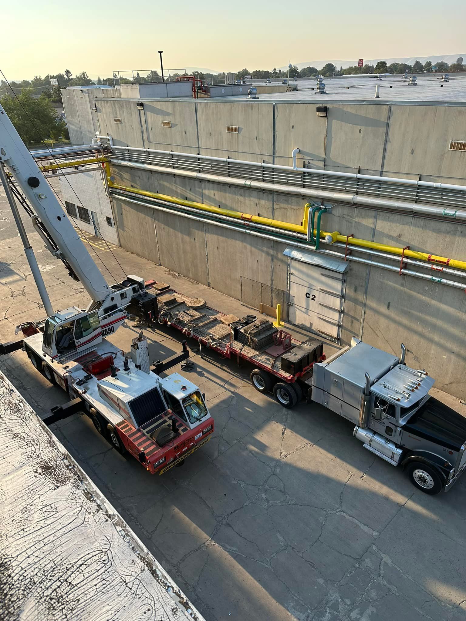 Crane and truck unloading equipment on a rooftop, sunny day.