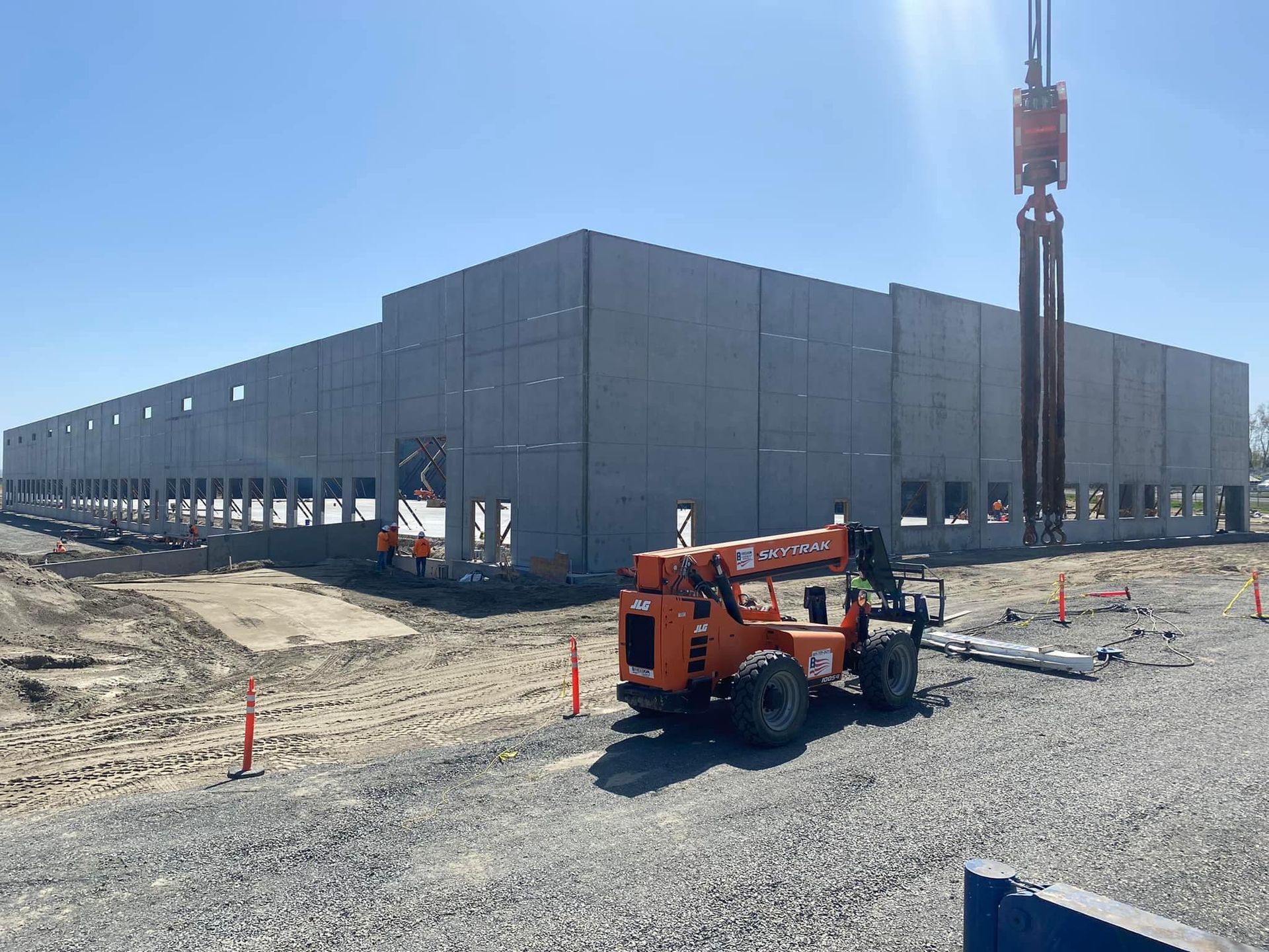 Construction site with large concrete building under construction. Crane and forklift visible.