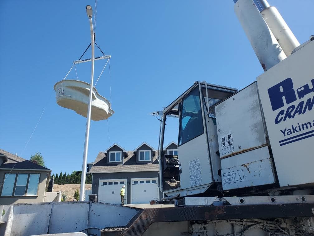 A crane lifting a small boat near a house on a sunny day.
