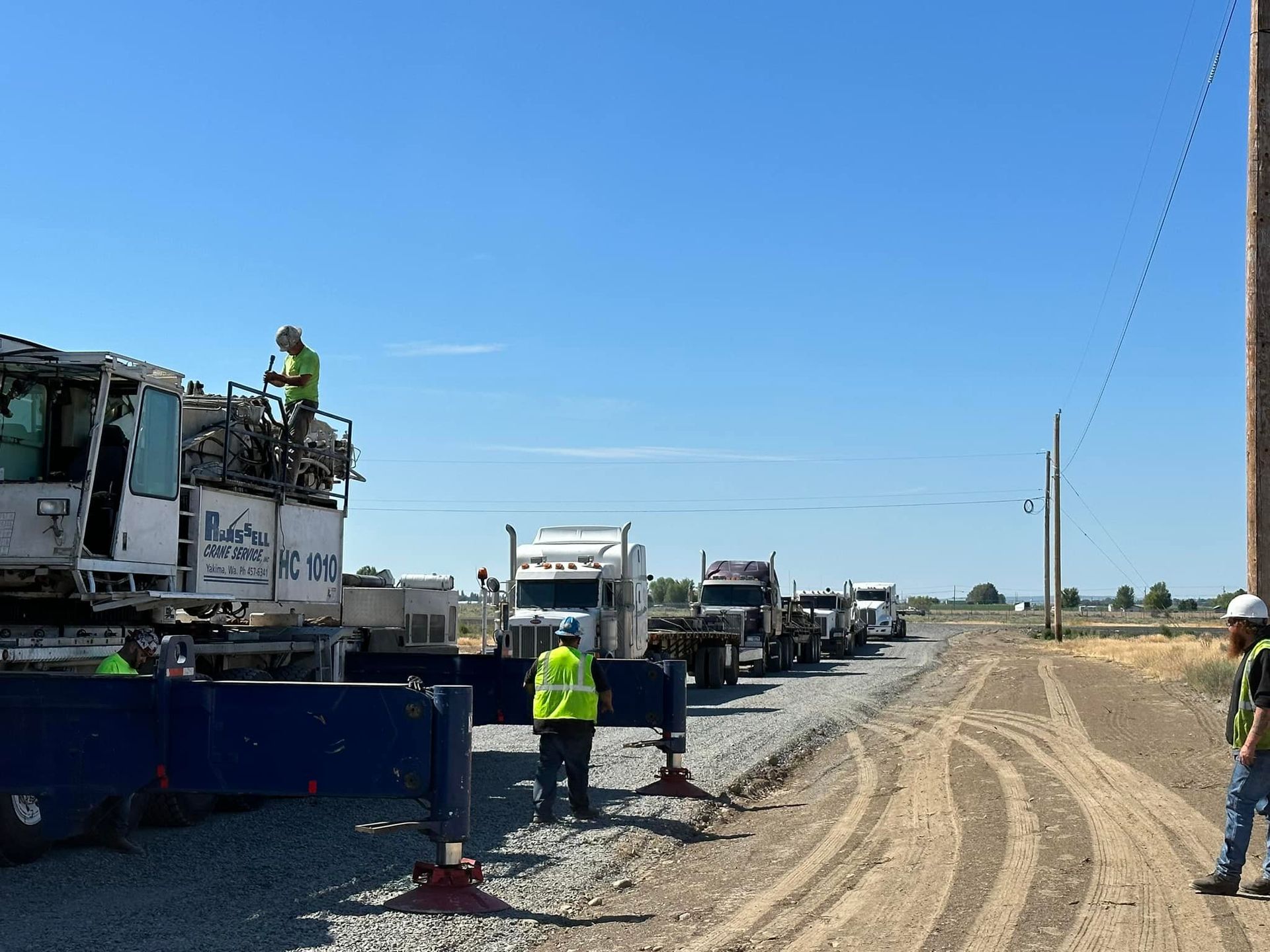 Construction workers near trucks on a gravel road under a blue sky.