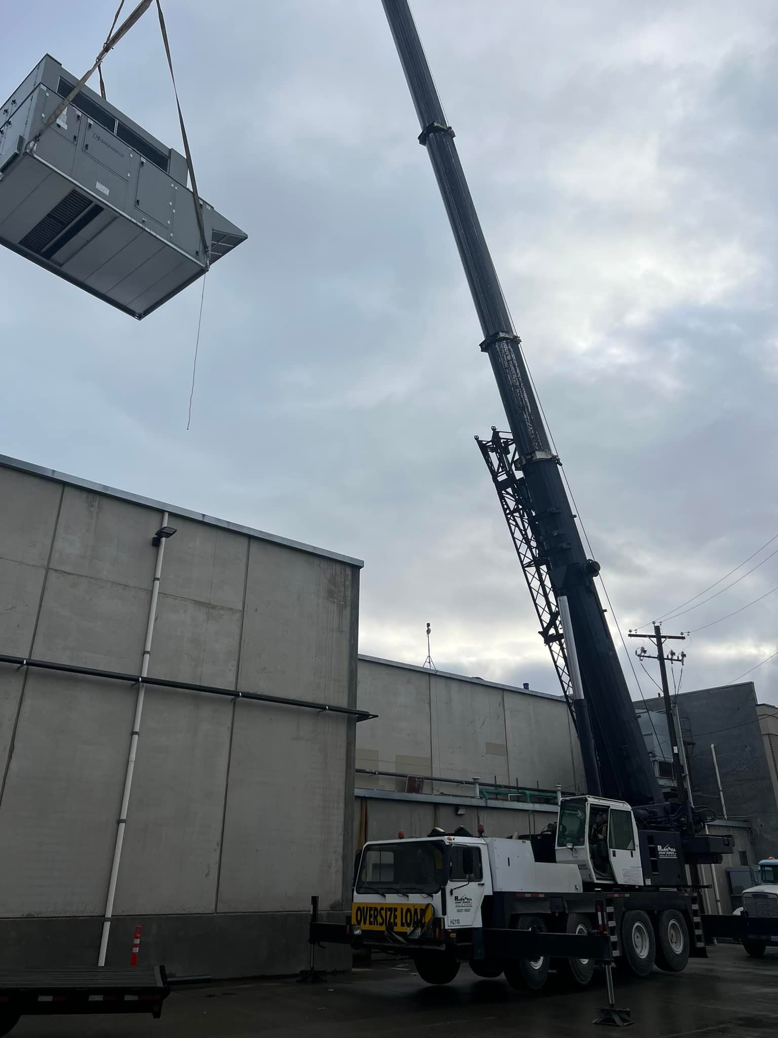 Crane lifting large HVAC unit onto a building on a cloudy day.