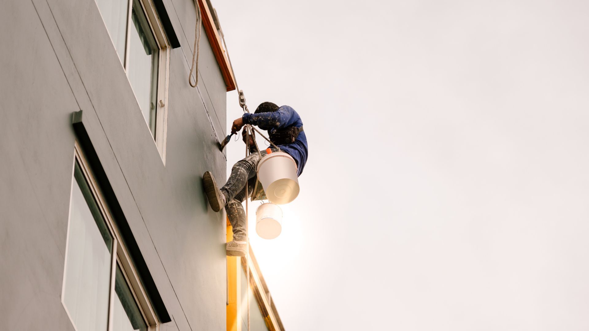 A man is painting the side of a building with a bucket.