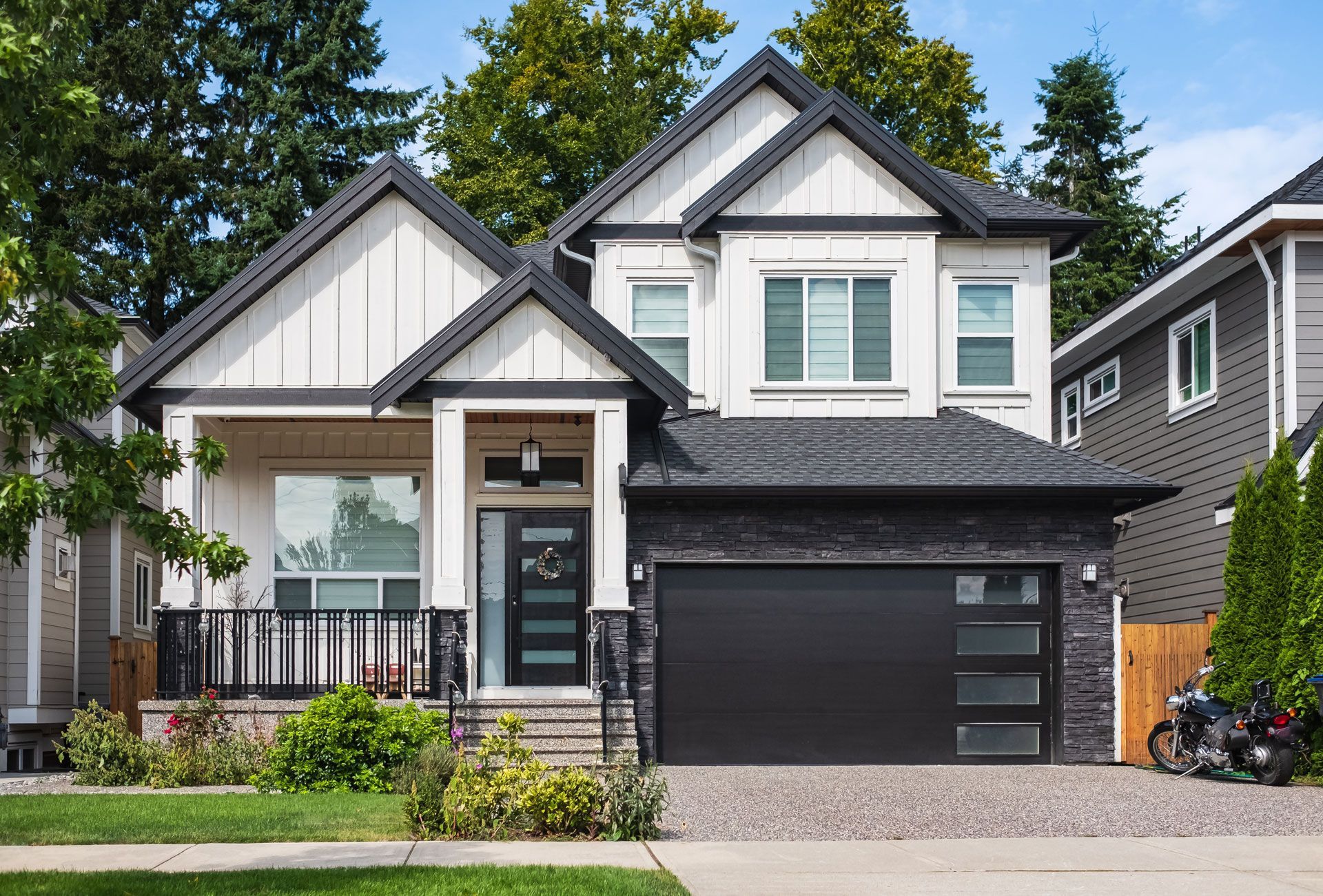 Modern two-story gray-and-white house with a black garage and front porch, seen from the street