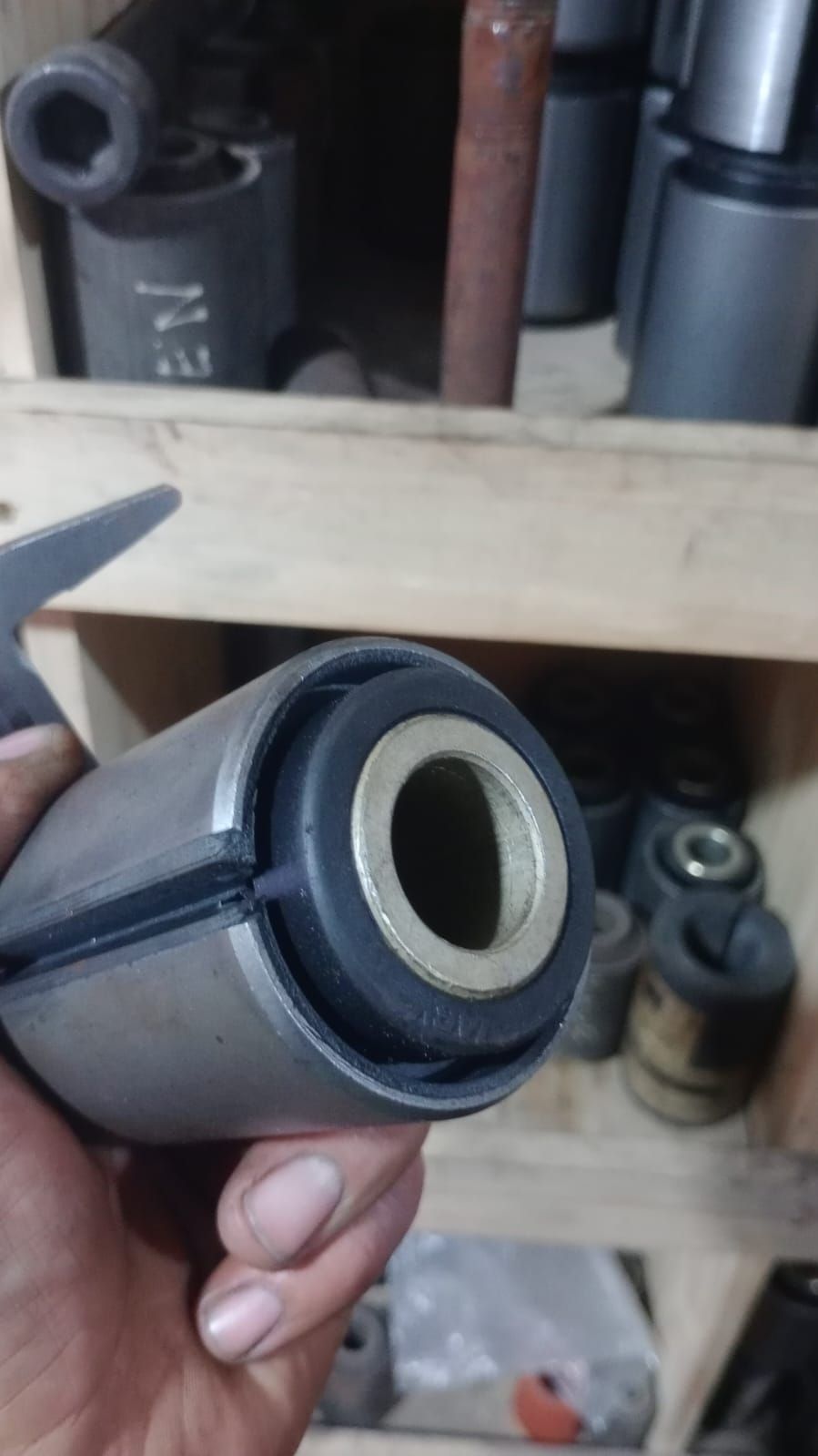 Primer plano de un casquillo de goma negro con un manguito metálico, sostenido en una mano en un entorno de taller.