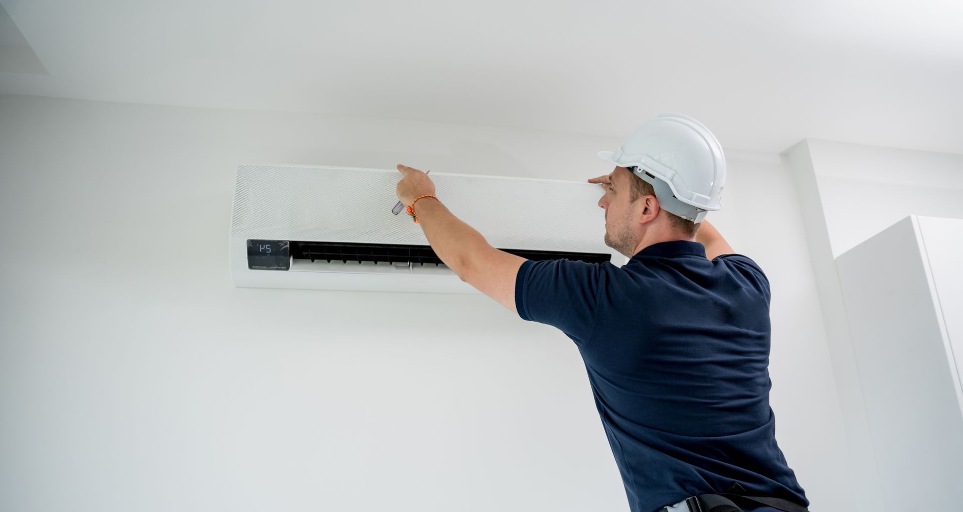 Worker in helmet adjusts wall-mounted AC unit in clean indoor space. Worker in helmet adjusts wall-mounted AC unit in clean indoor space.