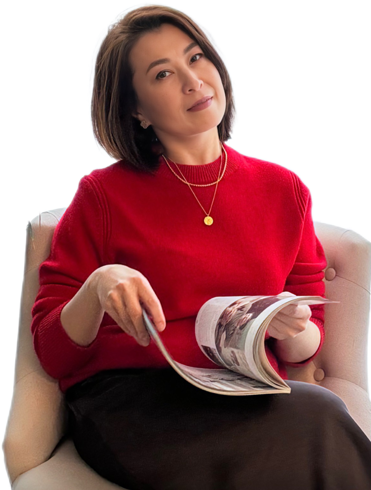 Woman in red sweater, sitting, holding magazine, smiling.