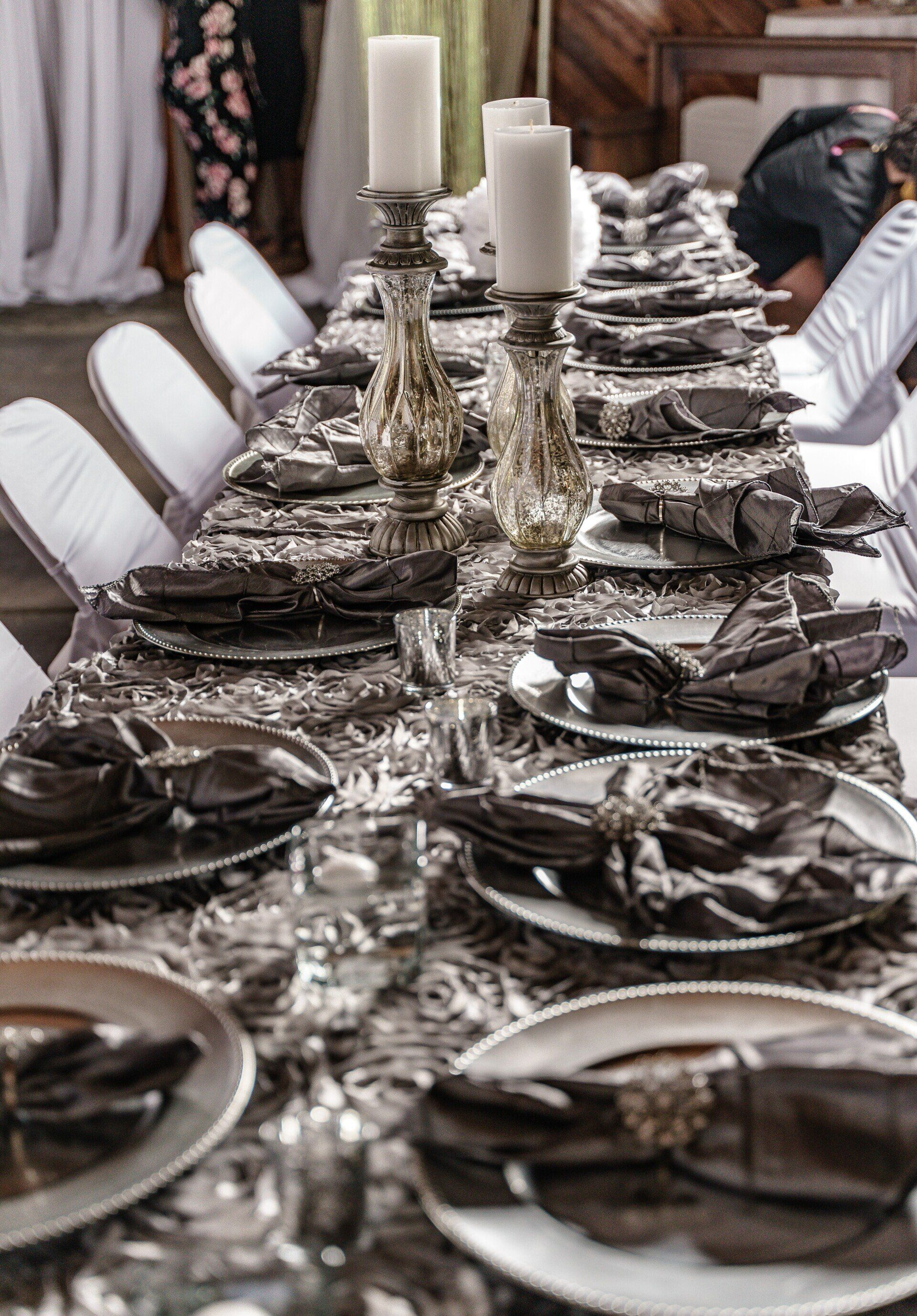 Elegant long dining table set with silver chargers, folded napkins, and white candles