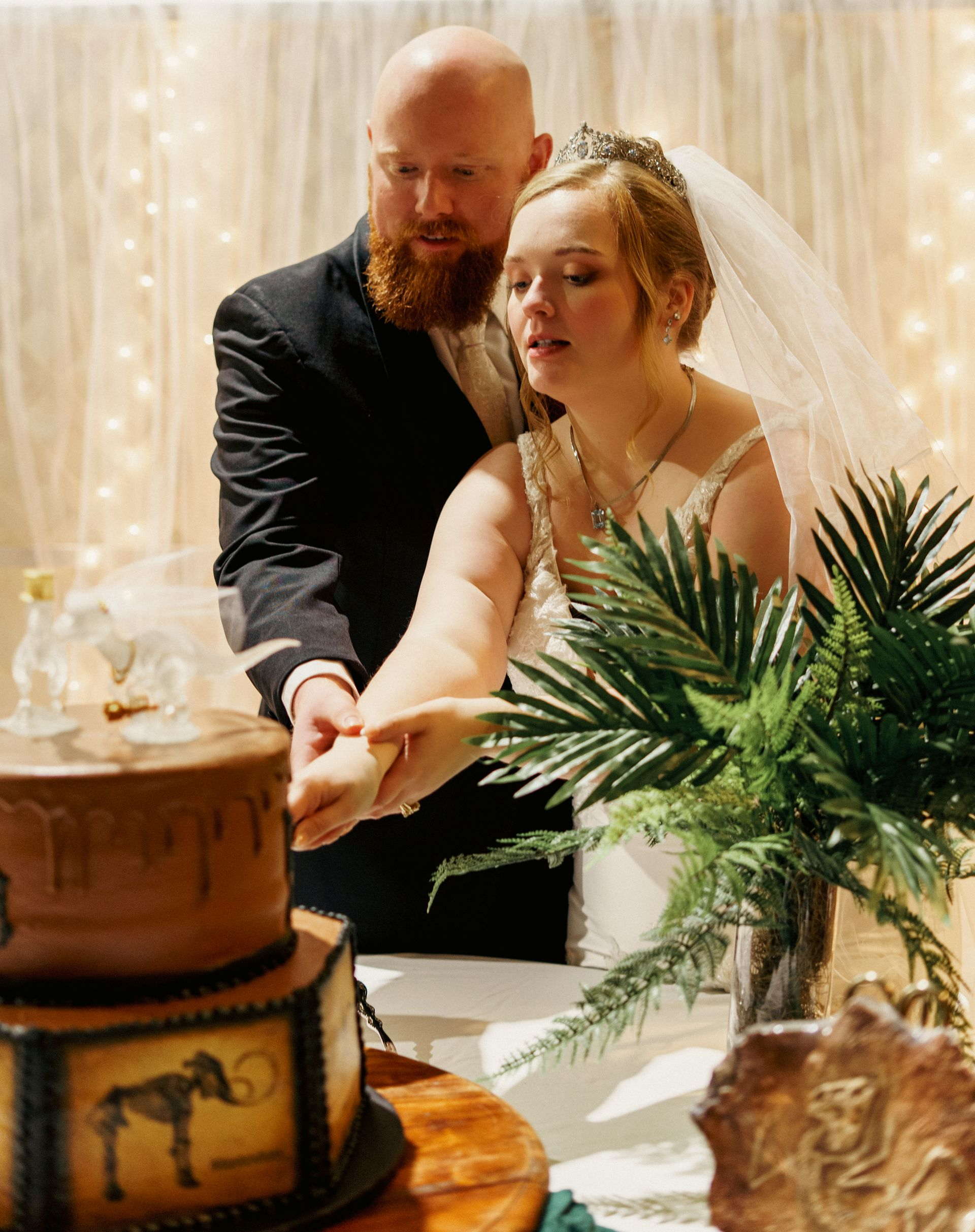Couple cutting a decorated cake at a warm, indoor celebration with fairy lights