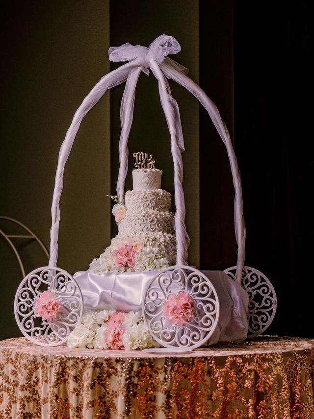 Decorative white wedding cake with pink flowers inside a white ribbon arch on a patterned table