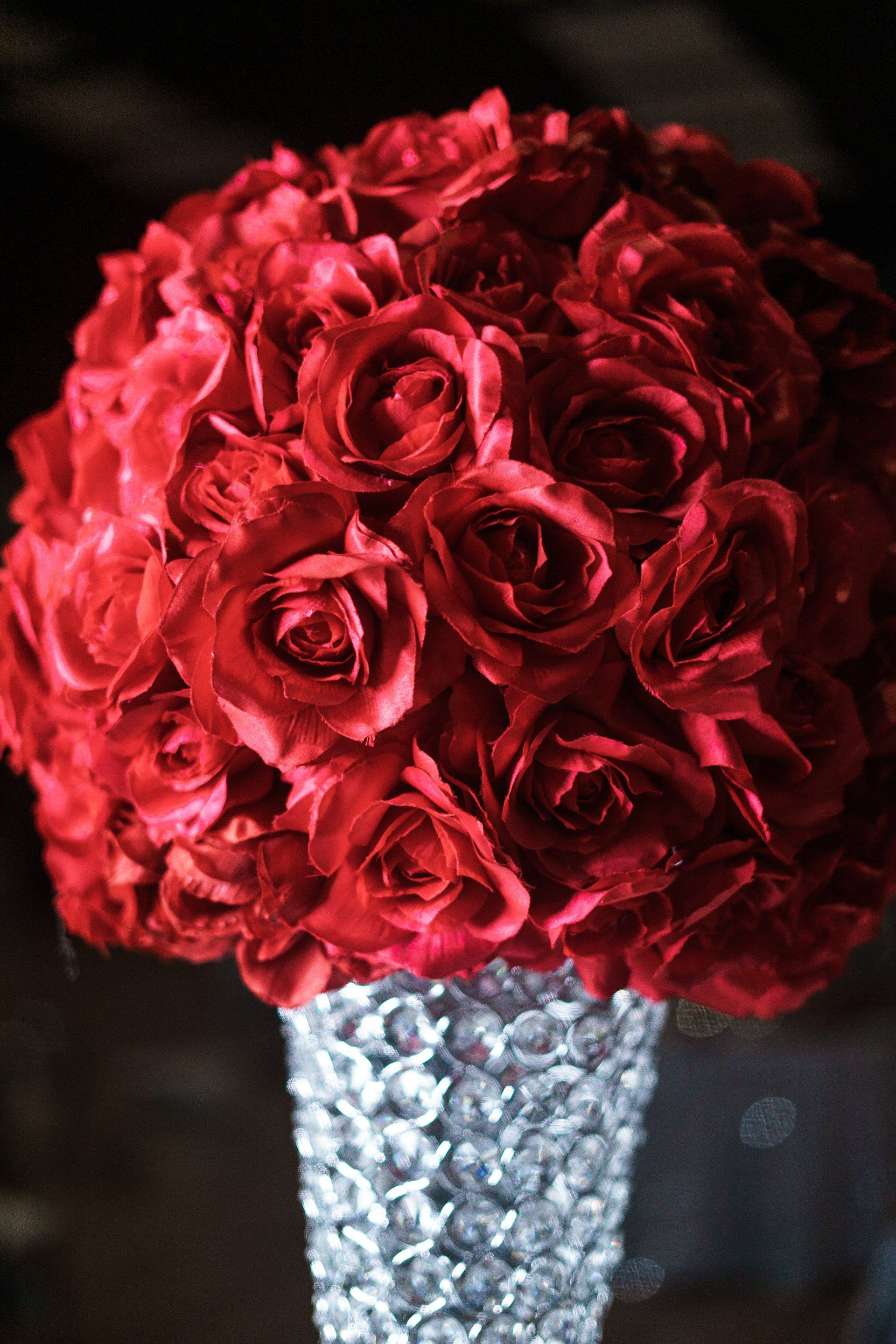 Red rose bouquet arranged in a silver vase on a dark background