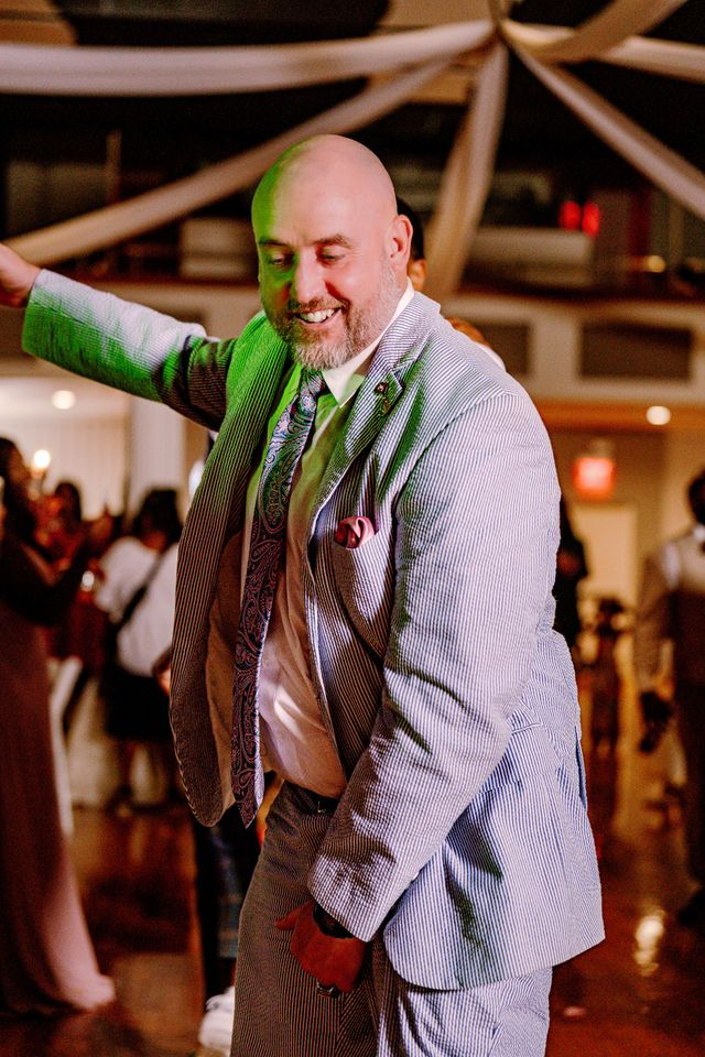 Man in a light suit dancing with one arm raised at an indoor event