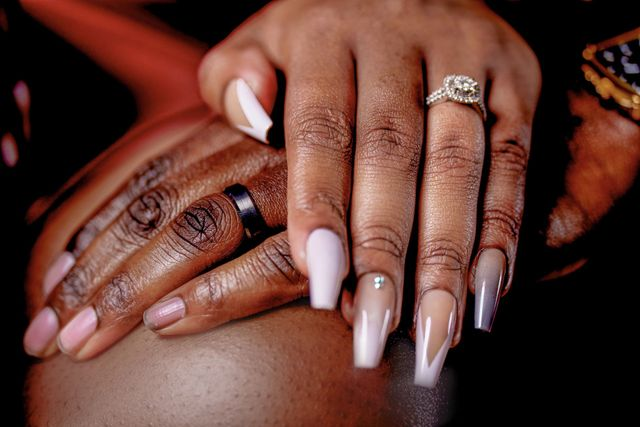 Hands with long white manicured nails and a silver ring resting on a person’s knee