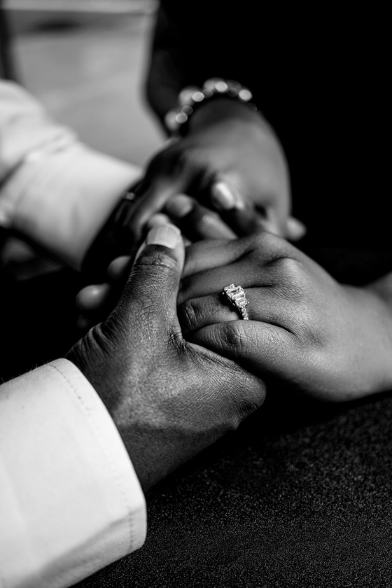 Hands clasped in prayer, one with a ring, in a black-and-white close-up