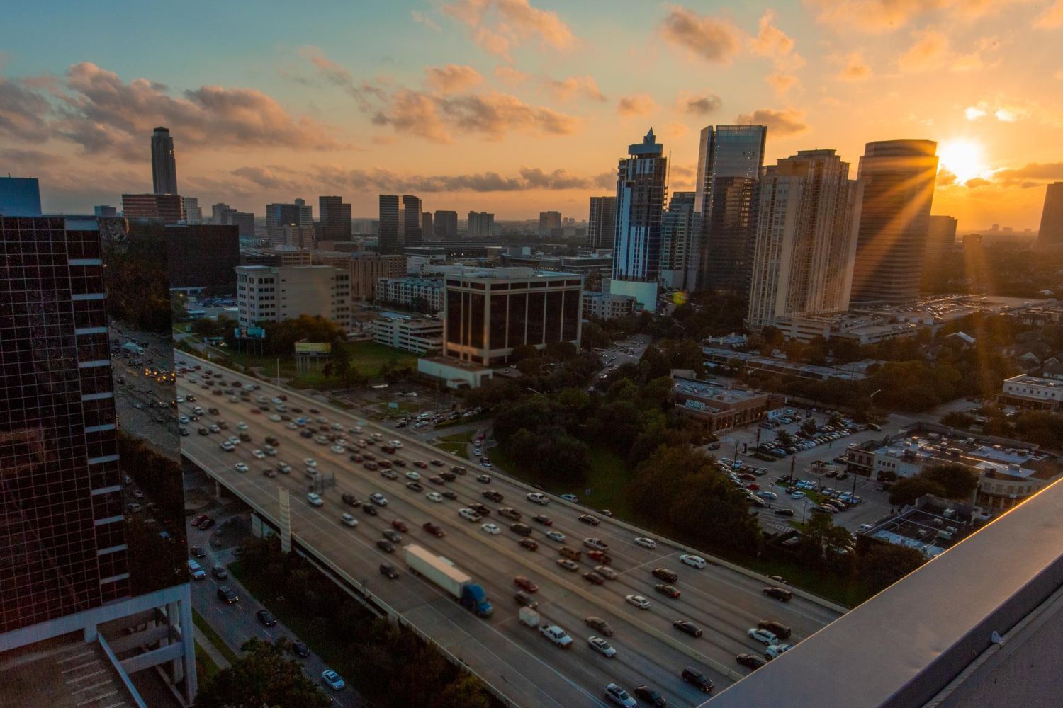 City skyline at sunset with a highway full of cars; golden light illuminates the buildings.