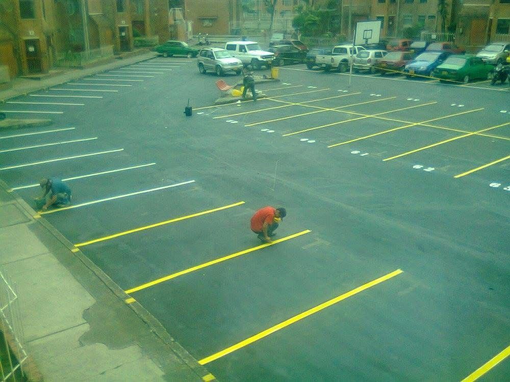 Aparcamiento vacío con líneas amarillas y varias personas marcando los espacios con tiza.